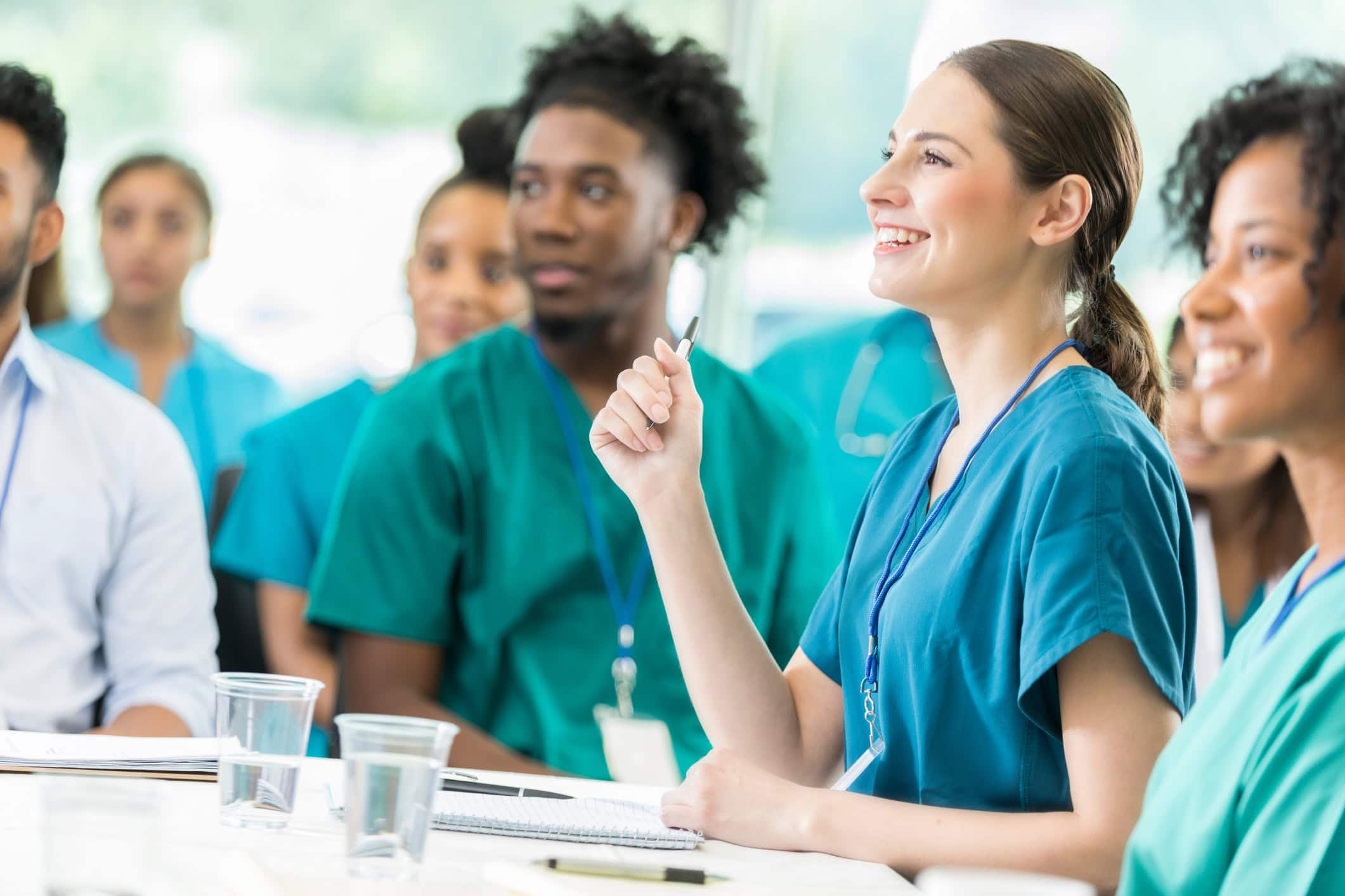 Cheerful young Hispanic female nurse attentively listens to a speaker during a medical seminar. Her colleagues are sitting next to her and are in the background.