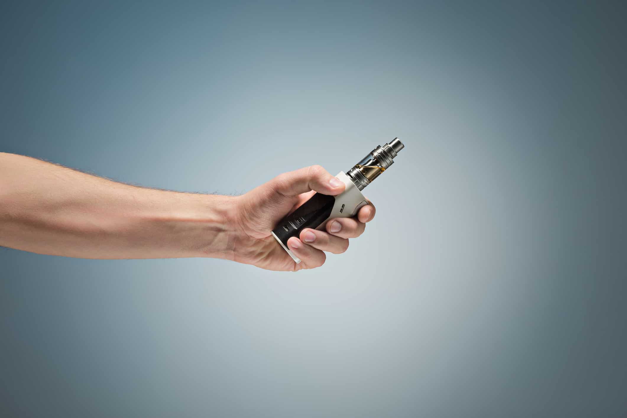 Hand holding an electronic cigarette over a studio background.