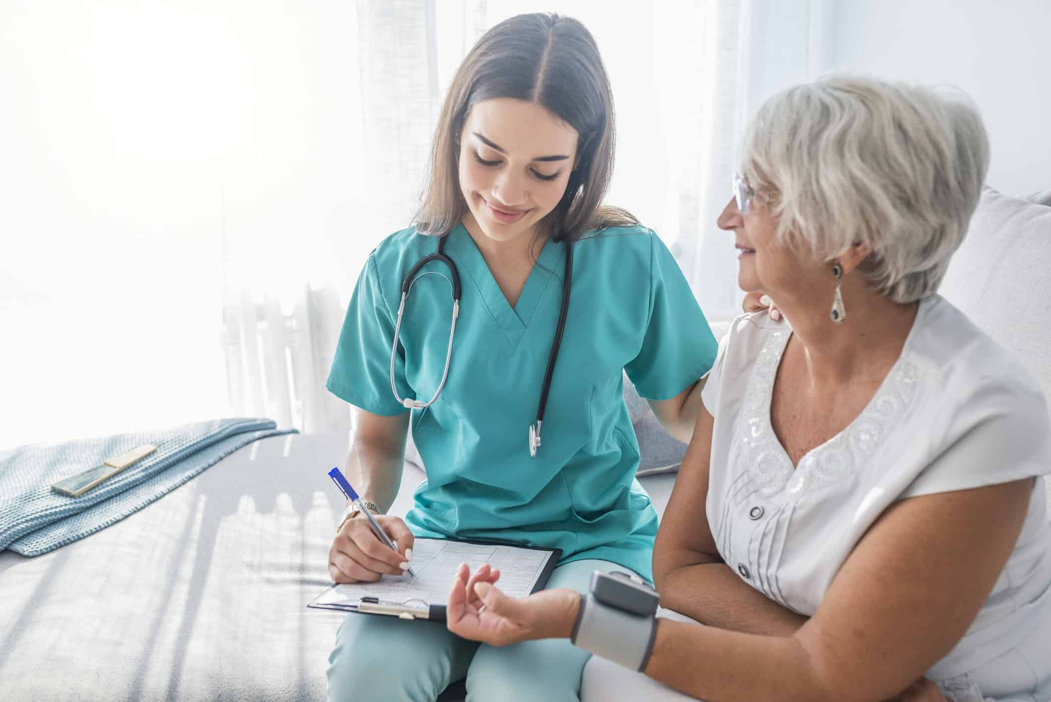 Nurse measuring blood pressure of senior woman at home. Smiling to each other. Young nurse measuring blood pressure of elderly woman at home. Doctor checking elderly woman's blood pressure