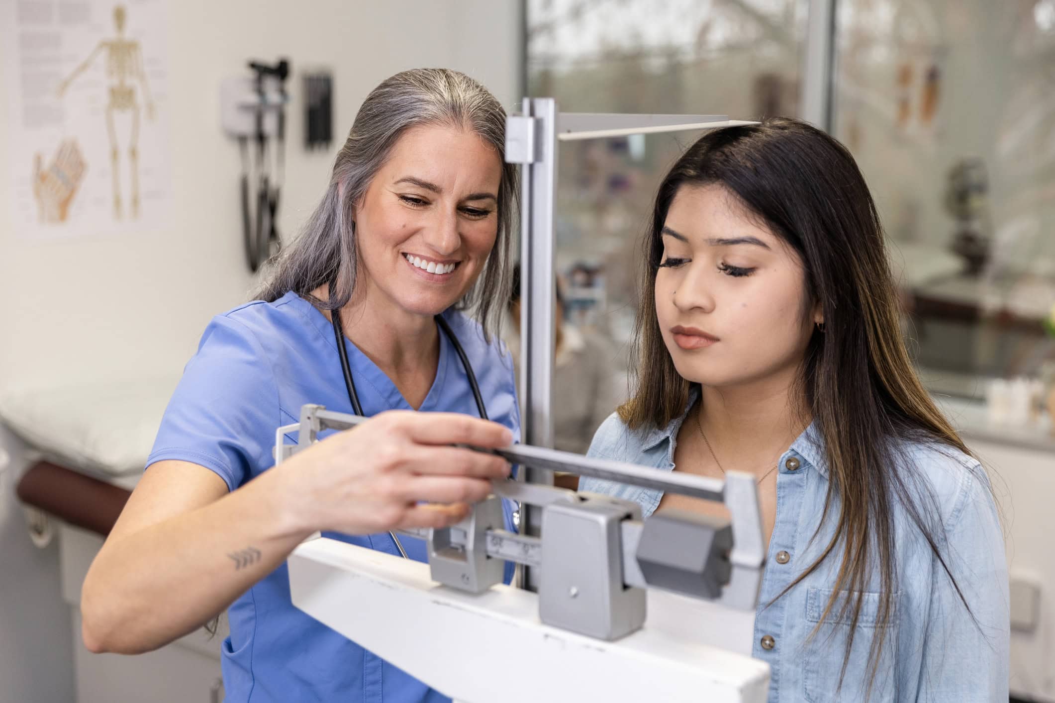 Female nurse smiles while checking teenage girl's weight and height Female nurse smiles while checking teenage girl's weight and height