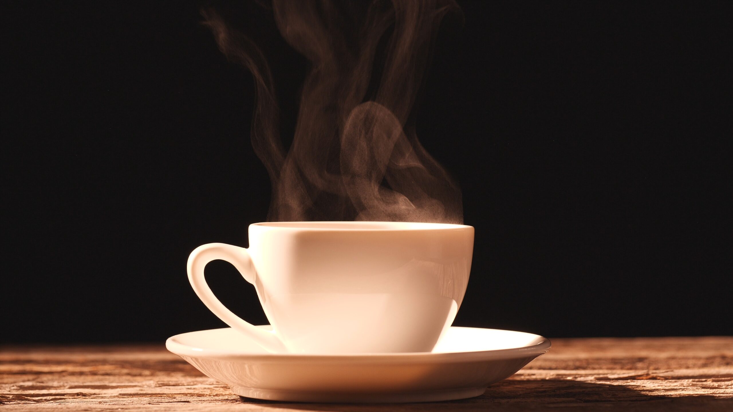 Coffee cup, Espresso, Americano, Black coffee. Close-up steam rises from cup of coffee with morning sunlight on old, vintage wood table, dark background. Concept breakfast, hot drink