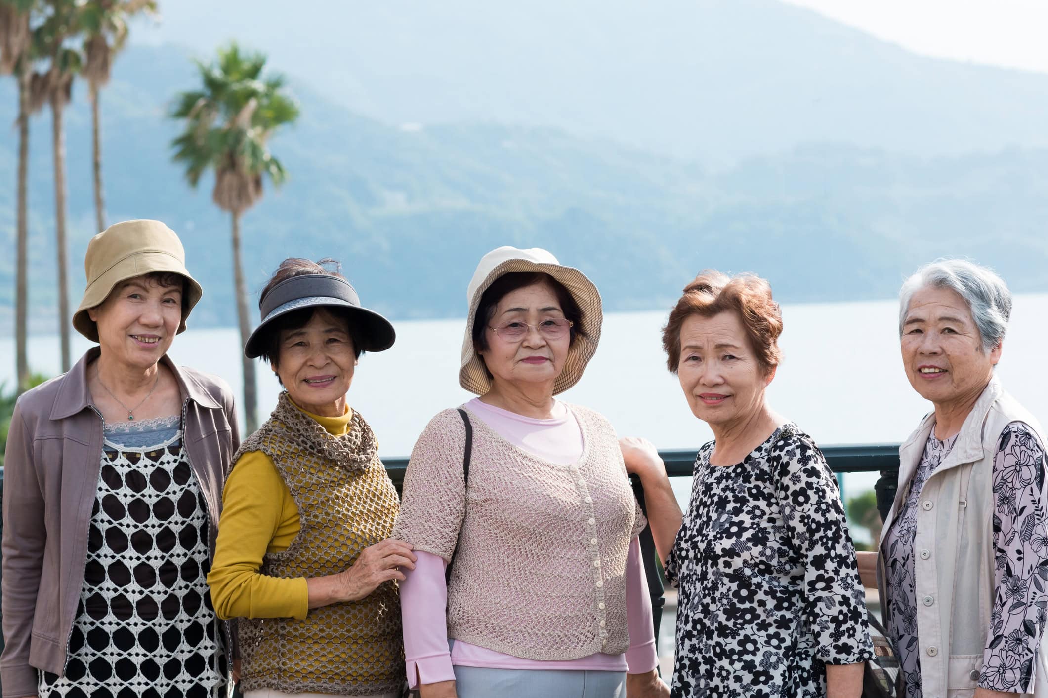 A group of older Asian women stand side by side in front of a body of water.