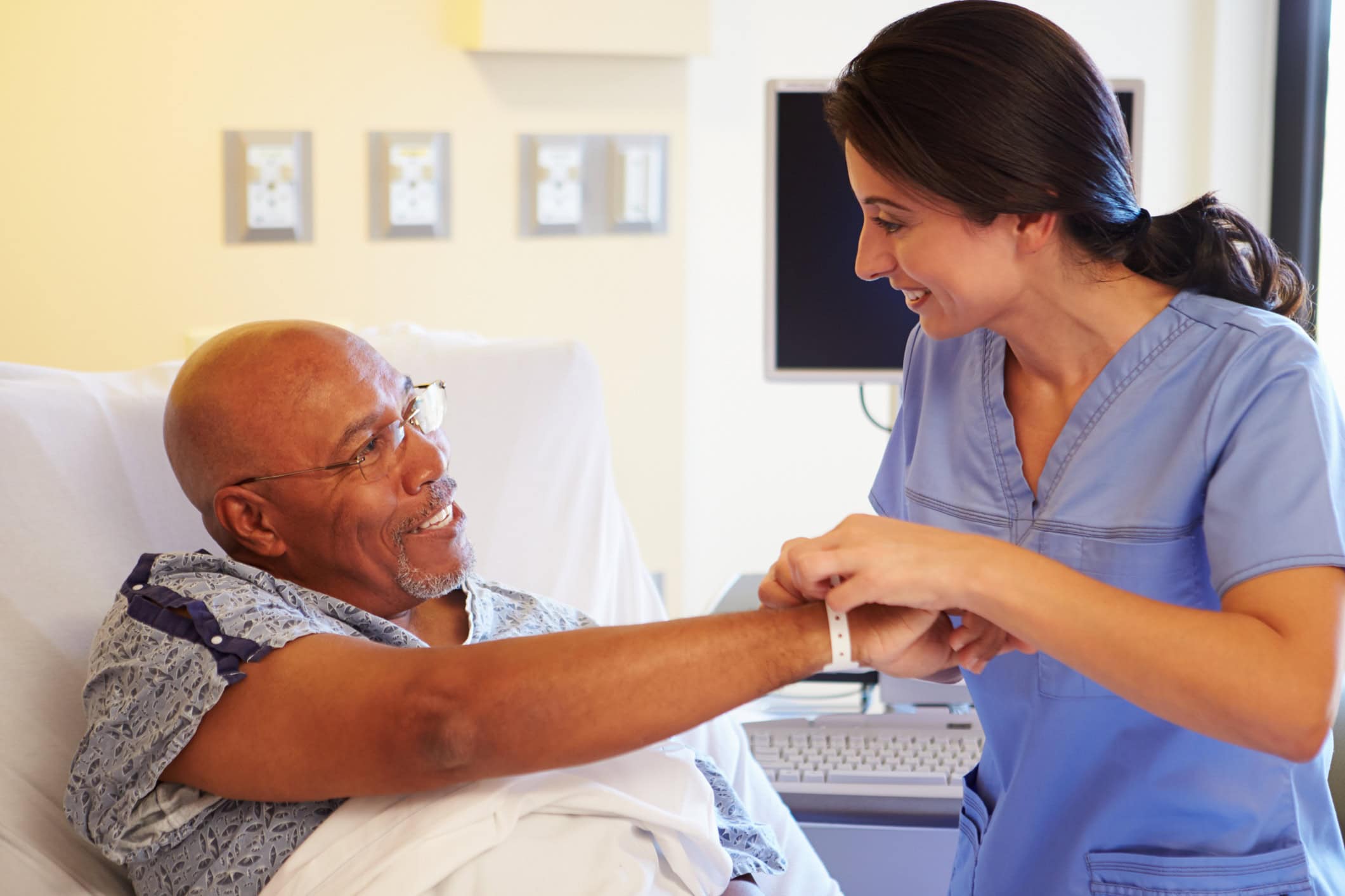 Happy Smiling Nurse Putting Wristband On Senior Male Patient In Hospital