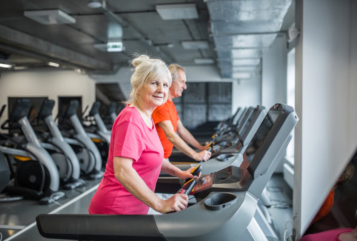 Portrait of smiling senior lady walking on treadmill at gym