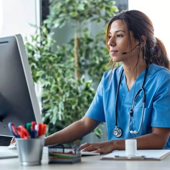 Nurse at desk telehealth office Shot of female doctor talking with earphone while explaining medical treatment to patient through a video call with computer in the